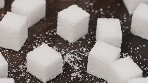 シュガーキューブはテーブルのクローズアップで回転する 白砂糖の多くは木の背景に滑らかな回転をしています 砂糖中毒 不健康な食事 過体重 糖尿病 肥満を概念する コピースペース — ストック動画