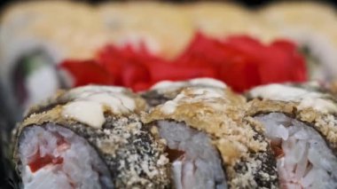 Suşi plastik bir teslimat kutusunda yuvarlanır. Yakın çekim döner. Yemeye hazır suşi kutusu ve farklı pişmiş lezzetli Japon dürümleri plastik kabın içinde dönüyor. Yemek teslimatı, paket yemek.