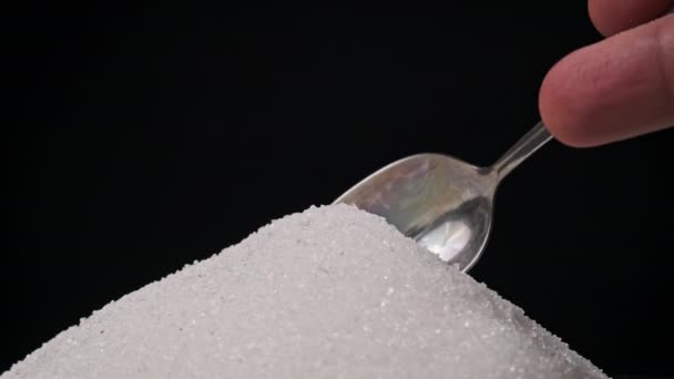 黒い背景の砂糖のヒープから砂糖でいっぱいのスプーンを得る スローモーションクローズアップ 白い粒状の砂糖のティースプーンを測定する 砂糖中毒 不健康な食事 太りすぎ 糖尿病 — ストック動画