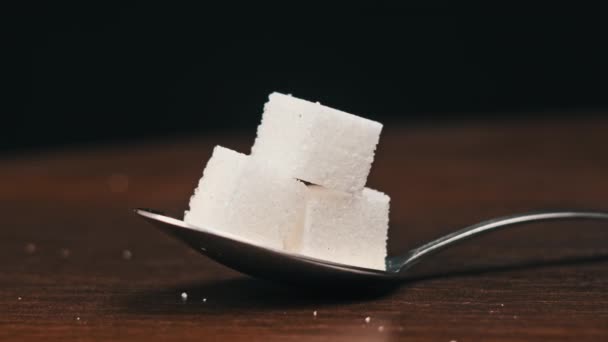 スプーン内の砂糖キューブは 黒い背景のクローズアップのテーブルの上に回転します 甘い白砂糖のヒープが付いている金属スプーン 砂糖中毒 不健康な食事 過体重 糖尿病 肥満を概念する — ストック動画