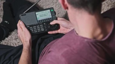 Adam, FM aralığında radyo istasyonlarının ve taramaların frekansını gösteren büyük dijital LCD ölçeğinde modern bir telsizi elinde tutuyor. Evdeki bir kanepede yatarak radyo alıcısını ayarlamak. Büyük rakamlar.