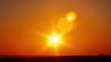 Saf turuncu gökyüzünde parıldayan mercekli muhteşem günbatımı zamanı. Ufuktan batan parlak güneş. Efsanevi, canlı bir renk. Zaman aşımı. Güzel gün batımı. 4K