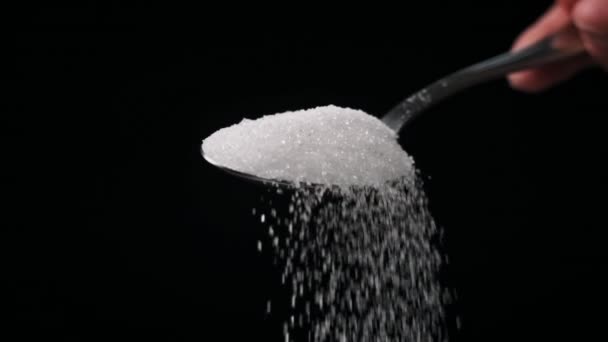 黒いバックグラウンドのスローモーションでフルスプーンから落ちる砂糖 クローズアップ 白い粒状糖のテーブルスプーン1杯を測定する 砂糖中毒 不健康な食事 太りすぎ 糖尿病 コピースペース — ストック動画