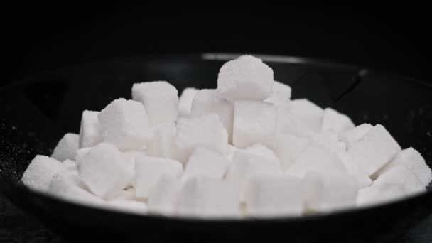 黑色盘子里的成堆的糖立方体旋转得很近 许多白色精致的糖块在桌子上旋转着 糖瘾的概念 不健康的饮食 糖尿病 复制空间 — 图库视频影像