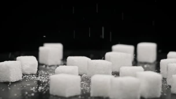シュガーキューブは回転テーブルの上に落ちてゆっくりと動きます 白い精製された砂糖の硬い部分は黒いテーブルに落ちます 砂糖中毒 不健康な食事 太りすぎ 糖尿病 コピースペース — ストック動画