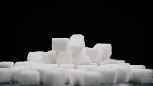 砂糖のキューブの山は 黒い背景のクローズアップで回転します 多くの白い精製された砂糖キューブがテーブルの上に回っています 砂糖中毒 不健康な食事 過体重 糖尿病 肥満を概念する コピースペース — ストック動画
