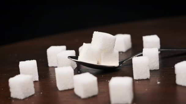 勺子中的糖立方体是桌子上的平滑旋转的特写 金属勺子和一堆甜白糖 概念糖瘾 不健康饮食 糖尿病和肥胖症 — 图库视频影像