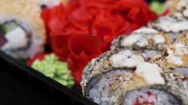 Suşi plastik bir teslimat kutusunda yuvarlanır. Yakın çekim döner. Yemeye hazır suşi kutusu ve farklı pişmiş lezzetli Japon dürümleri plastik kabın içinde dönüyor. Yemek teslimatı, paket yemek.