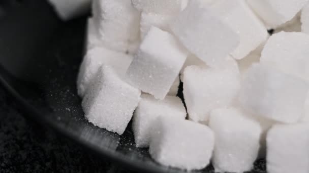 黑盘中的许多糖立方体旋转得很近 桌子上有一堆精炼的白色方块在纺纱 糖瘾的概念 不健康的饮食 糖尿病 复制空间 — 图库视频影像