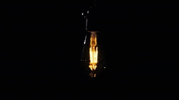 透明的经典灯泡挂在金属丝上 在黑色背景上摇曳 复制空间 现代白炽灯发光与温暖的灯丝 在黑暗中把Led钨关掉 古色古香4K — 图库视频影像
