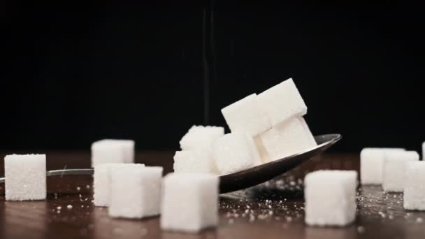 勺子中的糖立方体旋转在桌子上的黑色背景特写 金属勺子和一堆甜白糖 概念糖瘾 不健康饮食 糖尿病和肥胖症 — 图库视频影像