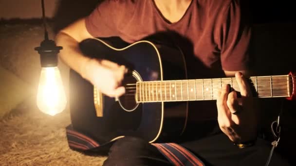 年轻人在光线温暖的黑暗房间里弹奏吉他 音乐家的剧本 在单一光源的照射下 投射出戏剧性的影子 在昏暗的光线下 吉他手 学唱歌 生活方式 — 图库视频影像