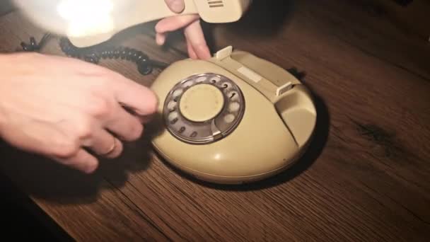 古いロータリー電話で電話番号をダイヤルする 木のテーブルの暖かいライトのハンドセットが付いているレトロな電話 ダイヤルディスク付きのヴィンテージのランドライン電話 男性の指はダイヤルディスク4Kを回転させます — ストック動画
