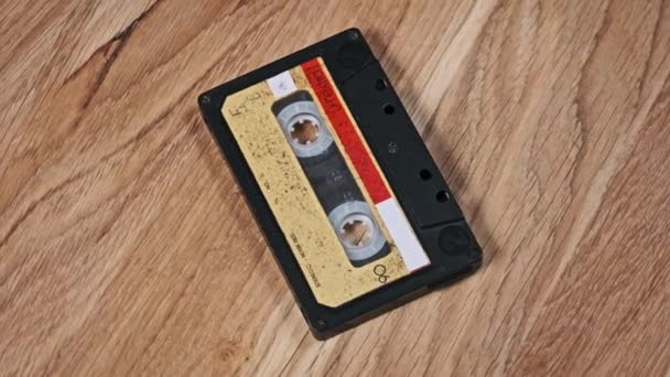 一盒录音带躺在一张木制桌子上旋转 古旧的录音带旋转宏观 旧盒式磁带躺在木制表面上 古典音乐过时的音乐80年代90年代怀旧 — 图库视频影像