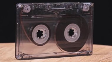 Şeffaf bir ses kaseti siyah arka plandaki ahşap bir masada dönüyor. Klasik ses bandı makroyu döndürür. Tahta bir yüzeyde duran eski bir ses kaydı. Klasik, müzik, 80 'ler, 90' lar. Nostalji.