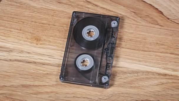 一个透明的盒式磁带躺在一张木制桌子上旋转 古旧的录音带旋转宏观 旧盒式磁带躺在木制表面上 古典音乐过时的音乐80年代90年代怀旧 — 图库视频影像