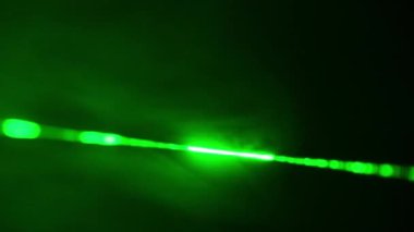Siyah bir arka planda, dumanlı yeşil lazer ışını. Siste parlayan bir lazer ışını. Karanlığı kesen yoğun, parlak lazer. Bilim kavramı, parti, araştırma.