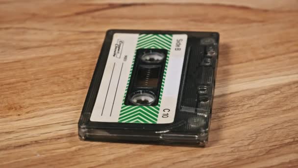 一盒录音带躺在一张木制桌子上旋转 古旧的录音带旋转宏观 旧盒式磁带躺在木制表面上 古典音乐过时的音乐80年代90年代怀旧 — 图库视频影像