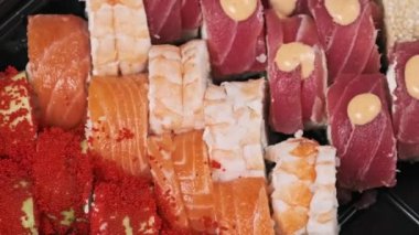 Suşi plastik bir kutuda yuvarlanır ve siyah arka planda yakın plan çekilir. Hazır suşi kutusu ve farklı lezzetli Japon dürümleri bir teslimat konteynerinde. Yemek teslimatı, paket yemek.