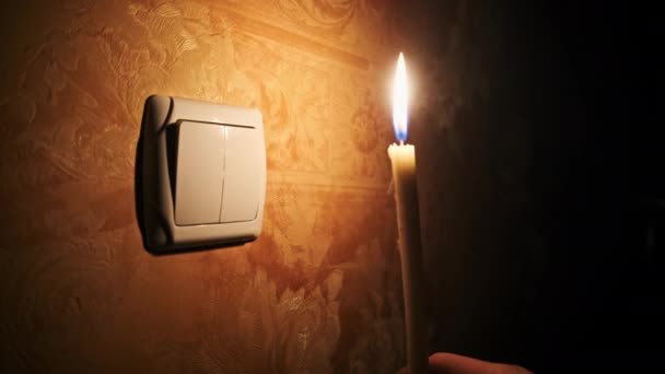 ブラックアウト 壁のライトスイッチの近くの暗い部屋でろうそくを燃やします エネルギー危機 停電など 電源に関する問題 男性の指が夜にライトスイッチをオンとオフにする — ストック動画