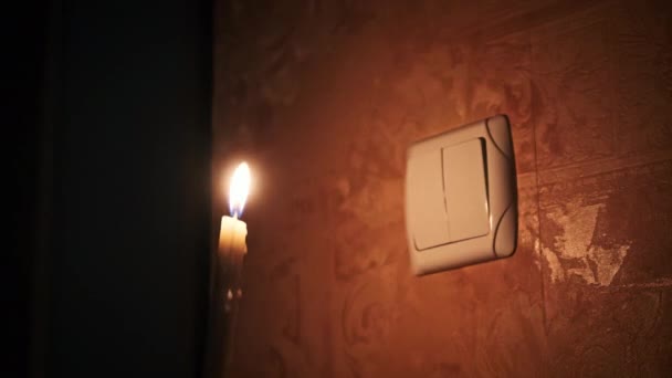 把点燃的蜡烛放在黑暗的房间里靠近电灯开关 能源危机或断电 电力供应方面的问题 男性手指打开和关闭电灯开关 — 图库视频影像