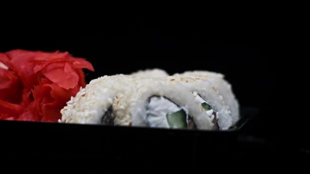 寿司卷在一个塑料盒中 在黑色背景上旋转特写 即食寿司盒 内装不同口味的日本卷 装在一个运送容器内 食物运送概念 外卖食物 — 图库视频影像