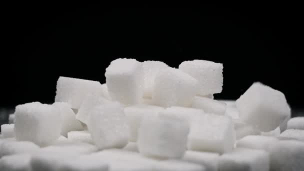 シュガーキューブは回転テーブルの上に落ちてゆっくりと動きます 白砂糖の硬い部分は黒い背景に落ちています 不健康な食事 太りすぎ 糖尿病 コピースペース — ストック動画