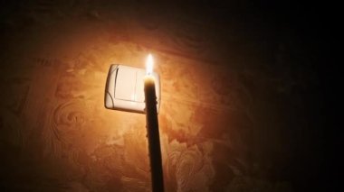 Elektrik kesintisi, karanlık bir odada yanan mum duvardaki ışık düğmesinin yanında. Elektrik kesintisi, enerji krizi veya elektrik kesintisi. Güç kaynağıyla ilgili sorunlar. Erkek parmak gece lamba düğmesini açıp kapatıyor.