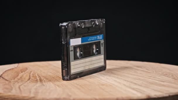一个盒式磁带在黑色背景特写的木制桌子上旋转 古旧的录音带旋转宏观 旧盒式磁带躺在木制表面上 古典音乐过时的音乐80年代90年代怀旧 — 图库视频影像