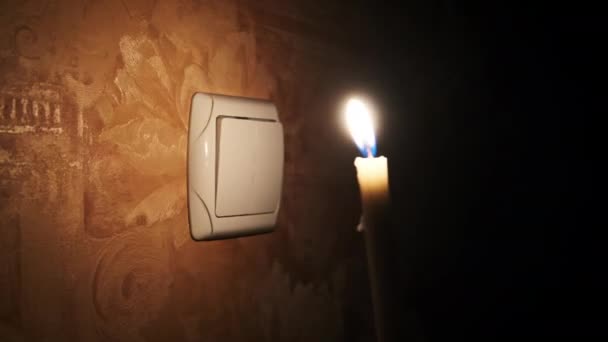 灯灭了 在墙头灯开关旁边的一间黑暗的房间里燃着蜡烛 能源危机或断电 电力供应方面的问题 男性手指打开和关闭电灯开关 — 图库视频影像