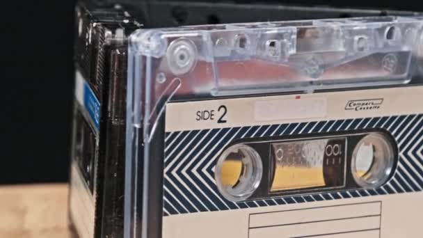 盒式磁带在黑色背景特写的木制桌子上旋转 古旧的录音带旋转宏观 旧盒式磁带躺在木制表面上 古典音乐过时的音乐80年代90年代怀旧 — 图库视频影像