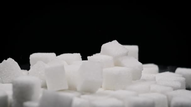 糖立方体以慢动作落在旋转桌子上 靠得很近 坚硬的白糖落在黑色的背景上 不健康的饮食 糖尿病 复制空间 — 图库视频影像