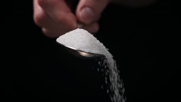 砂糖でいっぱいのスプーンは黒い背景のスローモーションに砂糖を入れ クローズアップします 白い粒状糖のテーブルスプーン1杯を測定する 砂糖中毒 不健康な食事 過体重 糖尿病肥満 — ストック動画