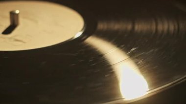 Retro turntable 'a yakın çekimde vinil çeviriyorum. Eski bir vinil kaydın eski bir plakta dönüşümlü görüntüsü. Vinil bir yüzeydeki lamba ışınının sıcak yansıması. Müzik tarihi, geçmişe dönük.