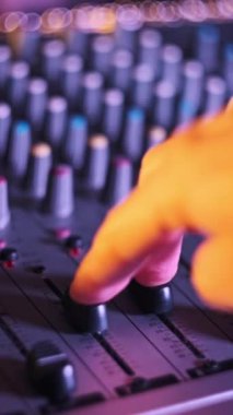 Dikey ses mühendisi faders 'ı neon ışıklı yakın plan ses mikserinde yukarı aşağı hareket ettirir. Erkek el karıştırma konsolunda ses düzeyini ayarlar. Renkli arkaplanda çalışan DJ müzik çalıyor