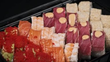 Suşi plastik bir teslimat kutusunda yuvarlanır. Yakın çekim döner. İçinde taze Japon dürümleri, zencefil ve plastik bir kapta dönen wasabi olan suşi kutusu. Yemek teslimatı, paket yemek.