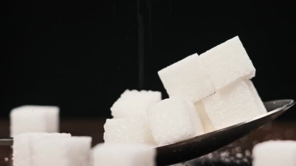 勺子中的糖立方体旋转在桌子上的黑色背景特写 金属勺子和一堆甜白糖 概念糖瘾 不健康饮食 糖尿病和肥胖症 — 图库视频影像