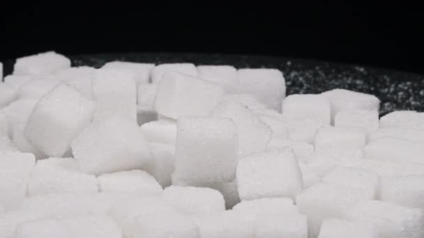 シュガーキューブは黒い背景のクローズアップで回転する 多くの白い精製された砂糖キューブがテーブルの上に回っています 砂糖中毒 不健康な食事 過体重 糖尿病 肥満の概念 コピースペース — ストック動画