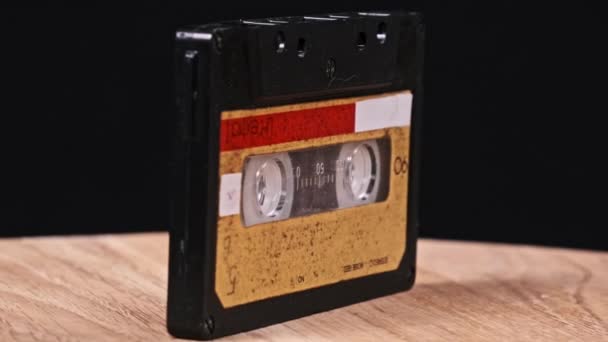Audiocassette Gira Sobre Una Mesa Madera Sobre Fondo Negro Cerca — Vídeos de Stock