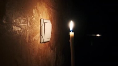 Elektrik kesintisi, karanlık bir odada yanan mum duvardaki ışık düğmesinin yanında. Elektrik kesintisi, enerji krizi veya elektrik kesintisi. Güç kaynağıyla ilgili sorunlar. Erkek parmak gece lamba düğmesini açıp kapatıyor.