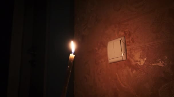 明かりのスイッチの近くの暗い部屋で燃えるろうそくを保持する エネルギー危機 停電など 電源に関する問題 男性の指が夜にライトスイッチをオンとオフにする — ストック動画