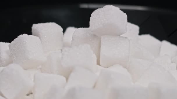 黑盘中的许多糖立方体旋转得很近 桌子上有一堆精炼的白色方块在纺纱 糖瘾的概念 不健康的饮食 糖尿病 复制空间 — 图库视频影像