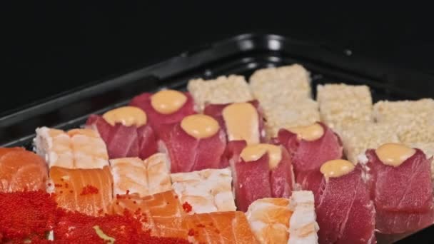回転配送ボックスに 黒い背景にセットされたお寿司ロール コンテナのクローズアップに日本製のロールが完成しました フードデリバリー おいしい食事 テイクアウトサービス — ストック動画