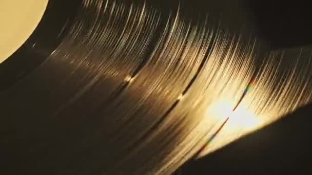 レトロターンテーブルのスピニングビニールクローズアップ ヴィンテージプレーヤーで回転する古いビニールのレコーディングのマクロショット ヴィンテージのビニールの表面にランプの光線の暖かい反射 音楽の歴史 レトロスタイル — ストック動画