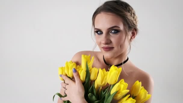 化粧している美しい若い女性は 白い背景に彼女の近くに黄色いチューリップの花束を保持しています スペースをコピーする カメラを一目見ると 謎が浮かび上がります スローモーション 4Kについて — ストック動画