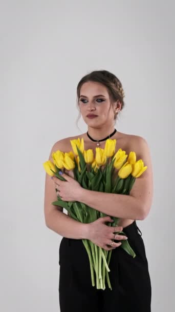 化粧している美しい若い女性は 白い背景に彼女の近くに黄色いチューリップの花束を保持しています スペースをコピーする カメラを一目見ると 謎が浮かび上がります スローモーション 4Kについて バーティカル — ストック動画