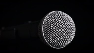 Dinamik el mikrofonu siyah arka planda döner. Mikrofon yavaşça kalkıyor. Mikrofon yüzeyinin yakın çekim krom şebekesi. Konsept kayıt stüdyosu, ses, podcast, karaoke, sesli kitap. Boşluğu kopyala