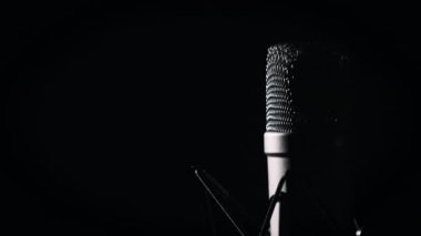 Bir stüdyo mikrofonu, arka planda siyah bir arka planda yakın planda döner. Yüzeyinde krom ızgarası olan daha yoğun bir mikrofon. Konsept kayıt stüdyosu, ses, podcast, karaoke, sesli kitap. Boşluğu kopyala