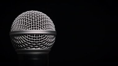 Ses mikrofonu yavaşça siyah bir arkaplanda döner. Dinamik yüzeyde yakın çekim krom ızgarası. Kopyalama. Konsept kayıt stüdyosu, ses, podcast, karaoke, sesli kitap.