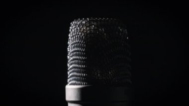 Stüdyo mikrofonu arka planda siyah bir arkaplanda döner. Çevresinde dönen mikrofon yüzeyinin krom şebekesine yakın çekim. Konsept kayıt stüdyosu, ses, podcast, karaoke, sesli kitap. Anlaşıldı.